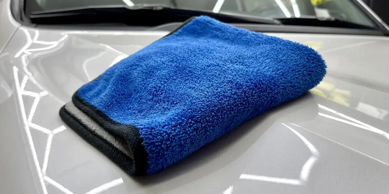En blå torkhandduk ligger på en skinande vit bilhuv. Perfekt för att torka av bilen efter tvätt.
