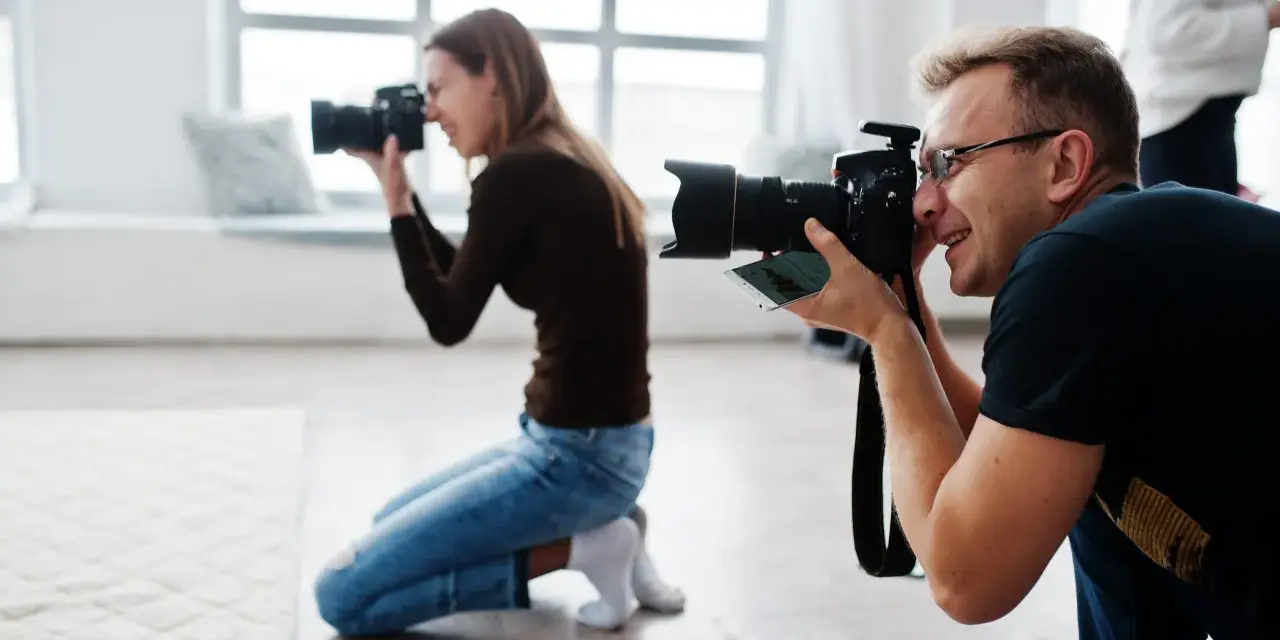 Dwóch fotografów klęczy i robi zdjęcia aparatem w jasnym studiu.