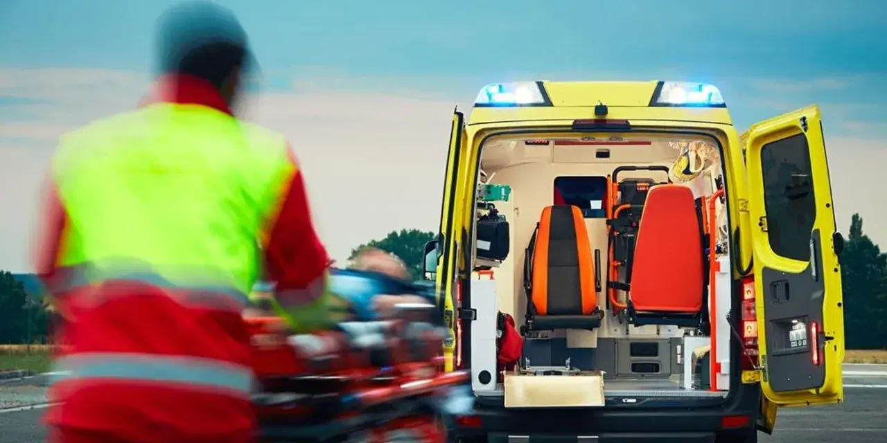 Ratownictwo medyczne w akcji. Ratownik w kamizelce odblaskowej transportuje pacjenta do karetki.
