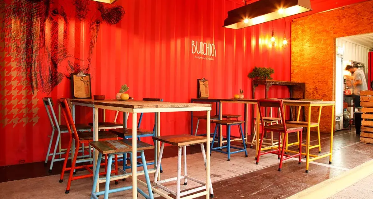 Decoración de restaurante con paredes rojas, mural de vaca y mesas coloridas.