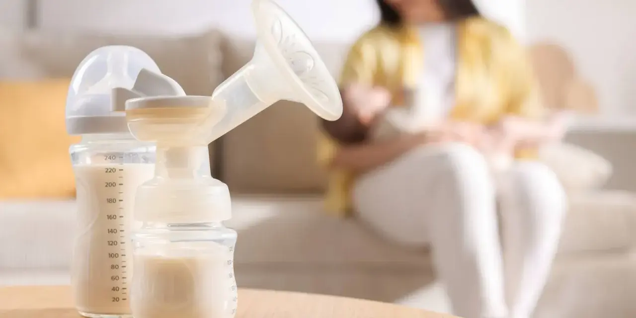 Biberon e tiralatte con latte materno, mentre una mamma allatta il suo bambino. Scopri come aumentare il latte materno in modo naturale.