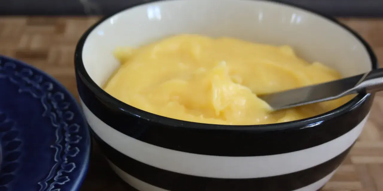 En skål med krämig, gul lemon curd, redo att bredas på en blå tallrik.