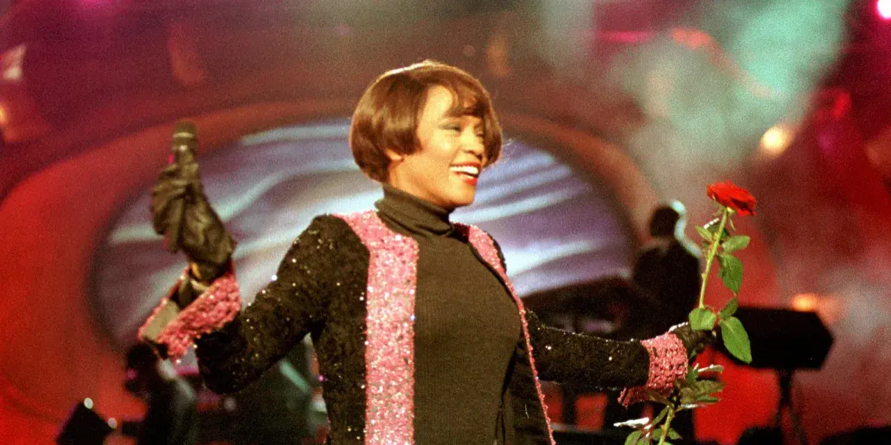 Whitney Houston z mikrofonem i czerwoną różą podczas niezapomnianego koncertu w Polsce.