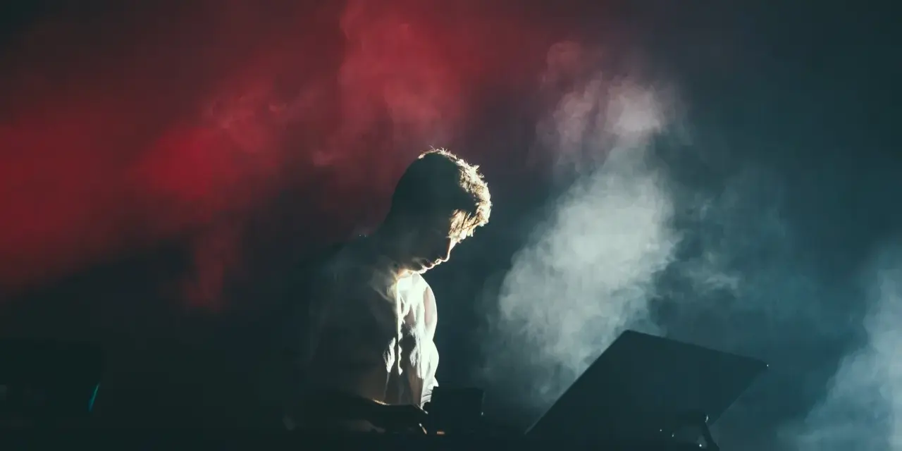Un DJ dans la fumée rouge et blanche, plongé dans sa musique. Combien de temps avant le traumatisme sonore ?