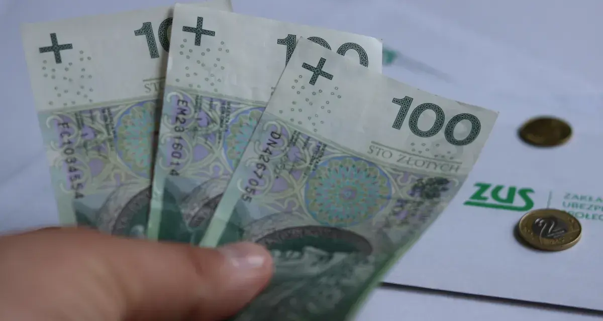 Trzy stuzłotowe banknoty w dłoni, obok dokument ZUS i monety. Czy to zapowiedź 30 krotności ZUS 2025?