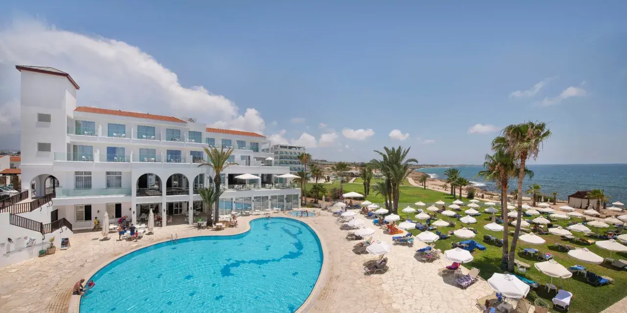 Słoneczny dzień w Akti Beach Village Resort. Basen, leżaki, palmy i morze - idealne miejsce na wakacje.