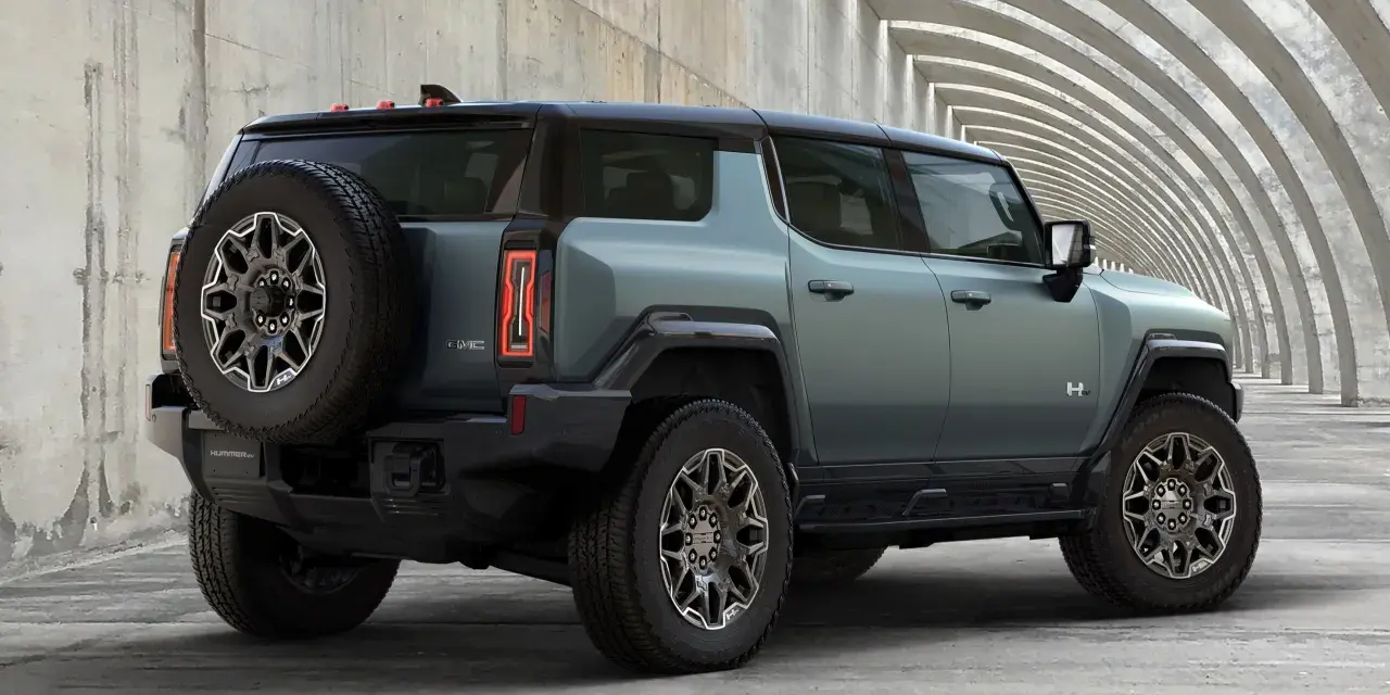 Zielony hummer elektryczny z kołem zapasowym z tyłu, zaparkowany przy betonowej konstrukcji z łukami.