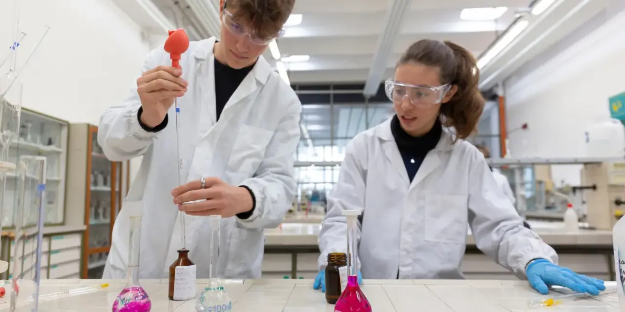 Ragazzi in camice bianco e occhiali protettivi eseguono esperimenti in laboratorio, un passo verso il loro futuro diploma perito chimico.