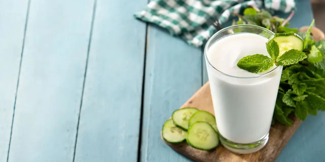 Szklanka białego napoju, idealna na kefir w ciąży, ozdobiona plasterkami ogórka i miętą.