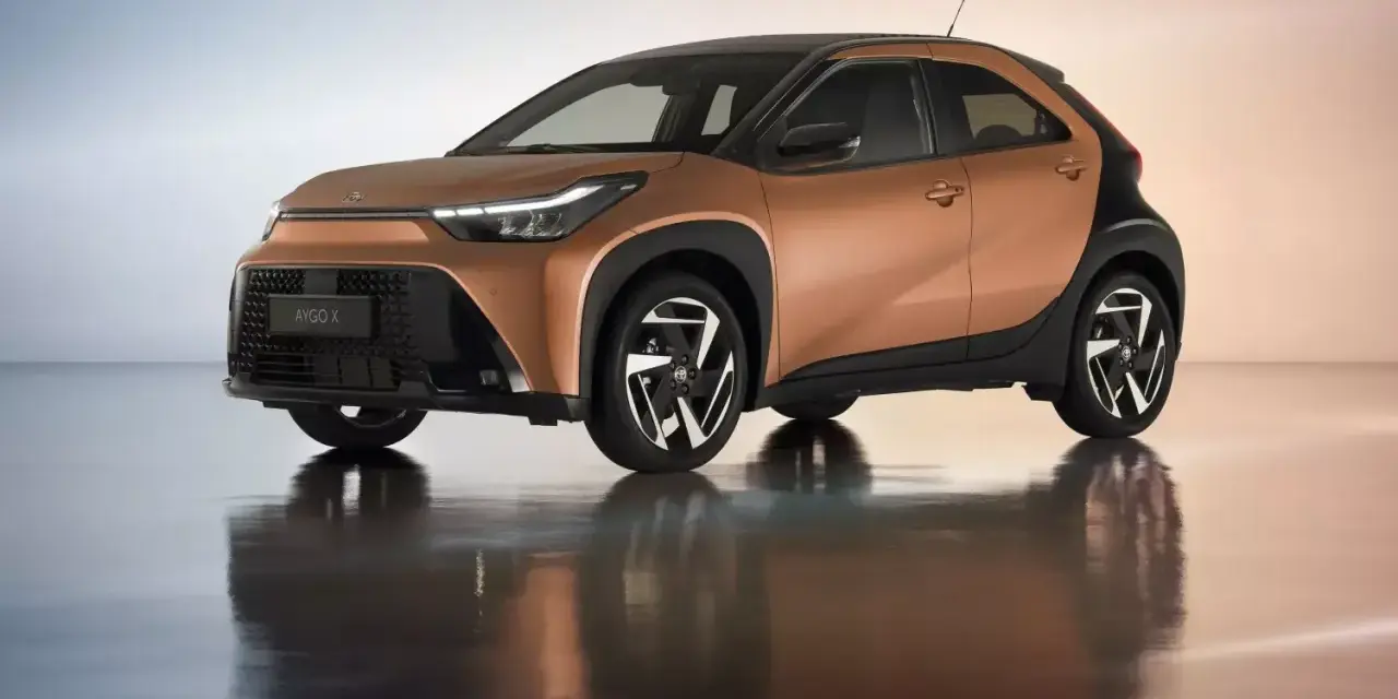Brązowy Toyota Aygo X z czarnym dachem i felgami na błyszczącym podłożu.