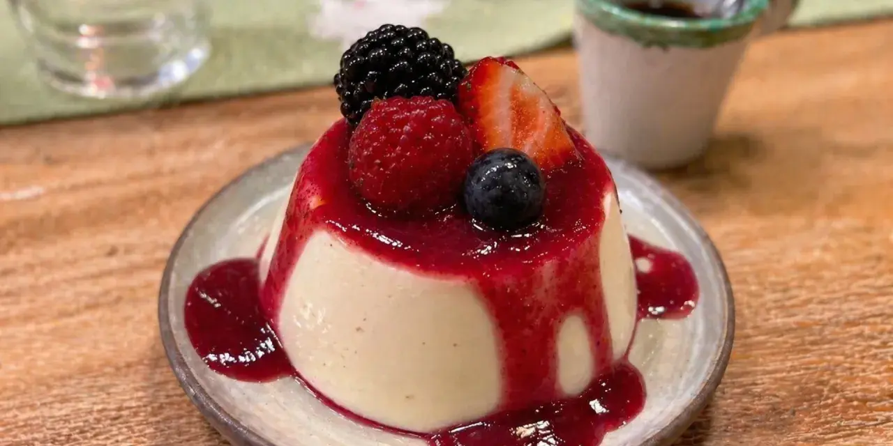 Cremige Panna Cotta mit Beeren und rotem Fruchtsirup auf einem Teller.