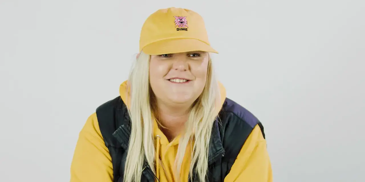 Frau mit gelber Kappe und Kapuzenpullover lächelt.