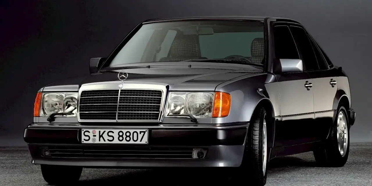 Klasyczny Mercedes W124 w ciemnym kolorze, z charakterystyczną atrapą chłodnicy i reflektorami. Ten model słynie z niezawodnych silników.