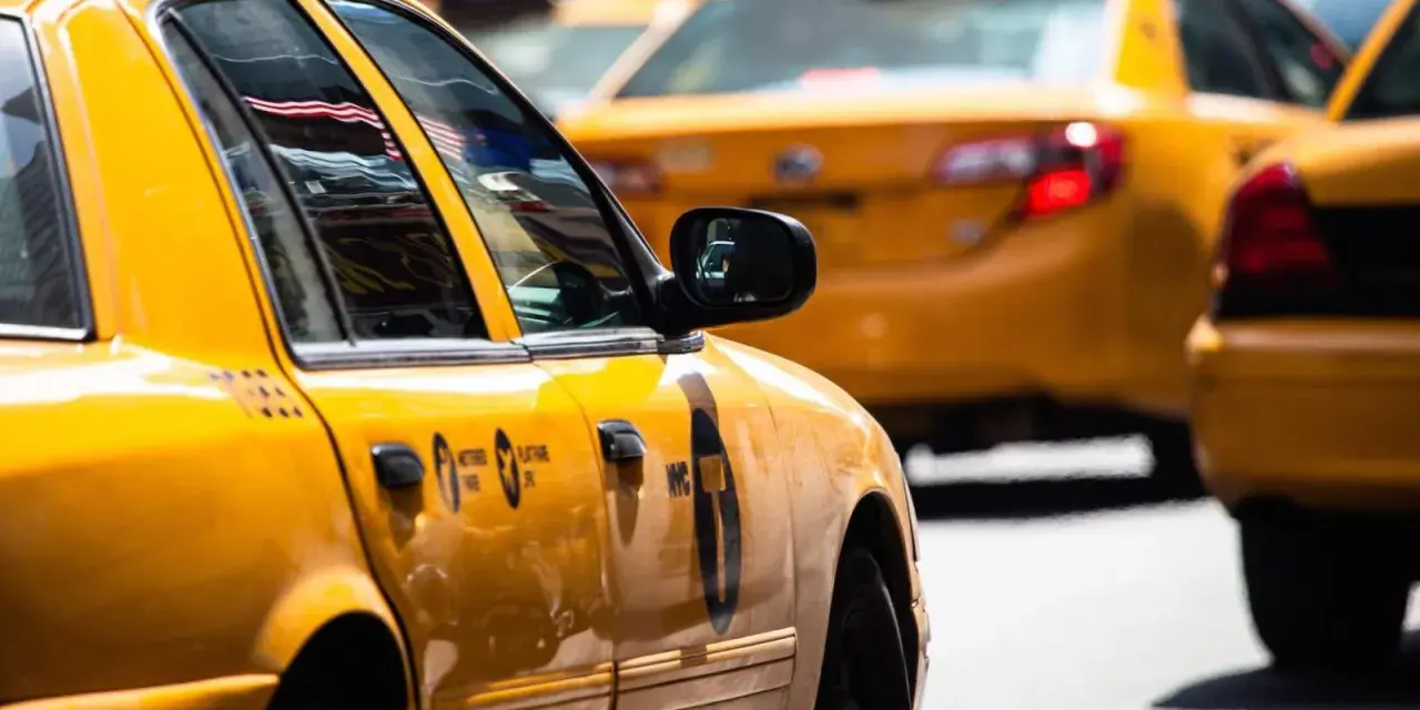 Gelbe Taxis in den USA, ein ikonischer Anblick. Die Spiegelung der US-Flagge im Fenster des vorderen Taxis.