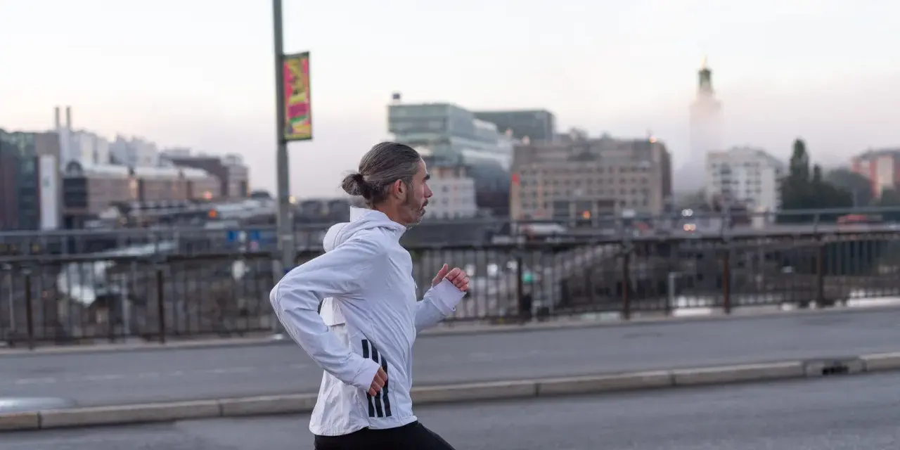 Man med hästsvans springer på en bro i Stockholm, klädd i adidas halvmarathon-kläder.
