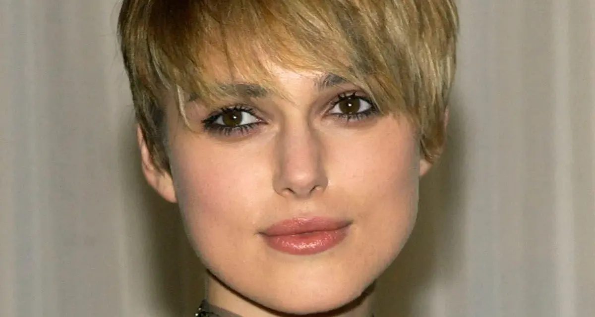 Primo piano di una donna con capelli biondi e tagli corti belli, trucco occhi marcato e un choker decorato.