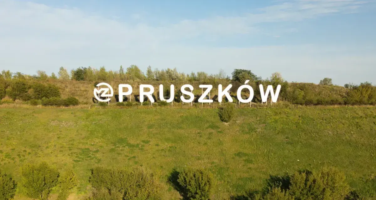 Napis "Pruszków" na tle zielonego wzgórza. Zastanawiasz się nad cenami mieszkań Pruszków?