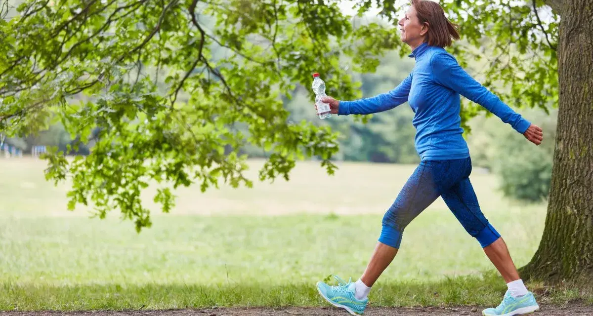 Femme souriante en tenue de sport bleue, profitant de 30 minutes de marche rapide par jour dans un parc verdoyant.