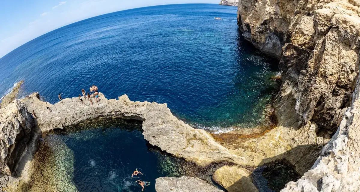 Ludzie kąpią się w naturalnym basenie skalnym, znanym jako blue hole, otoczonym klifami i turkusowym morzem.