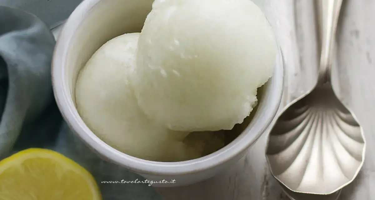 Coppetta di sorbetto al limone, fresca e dissetante, con limone fresco e cucchiaio decorato.