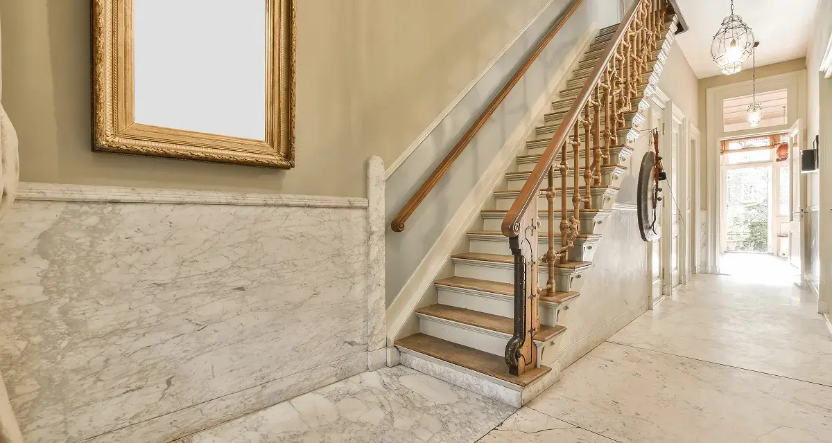 Elegante rellano de escalera comunitaria con mármol y un cuadro dorado. Ideas para decorar rellano escalera comunidad.