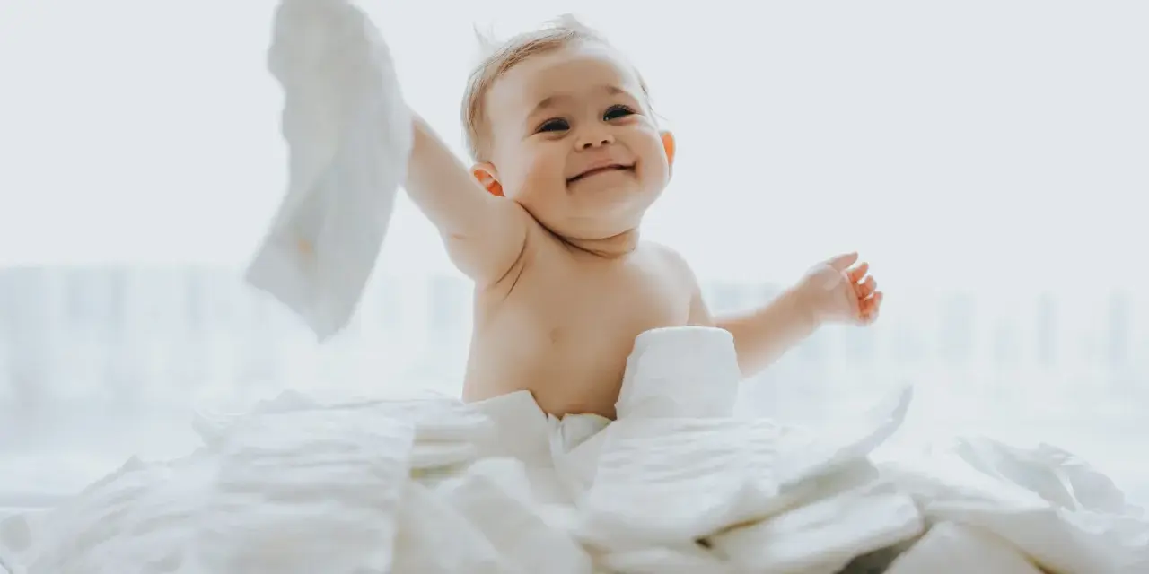 Uśmiechnięty bobas otoczony stertą pieluch. Zastanawiasz się, jakie pieluchy dla noworodka będą najlepsze?