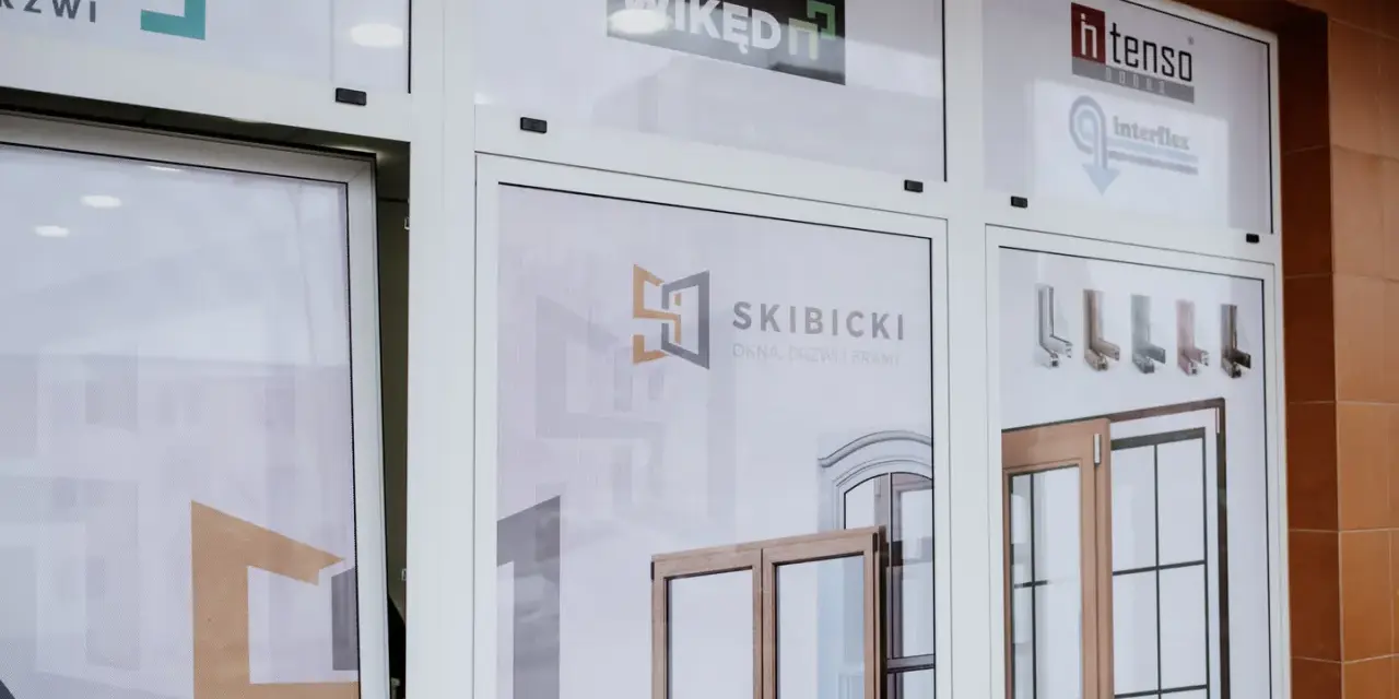 Witryna salonu okien i drzwi z logotypami firm i zdjęciami produktów.