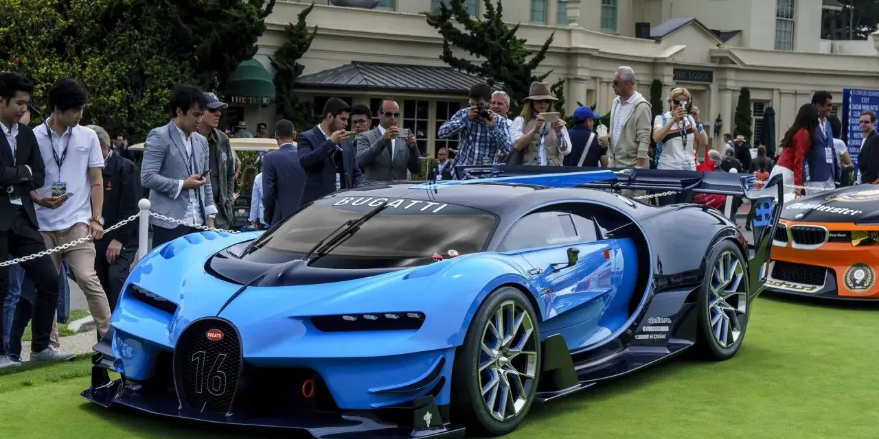 Niebieski Bugatti Veyron z numerem 16 na masce, otoczony tłumem ludzi robiących zdjęcia, na tle eleganckiego budynku.