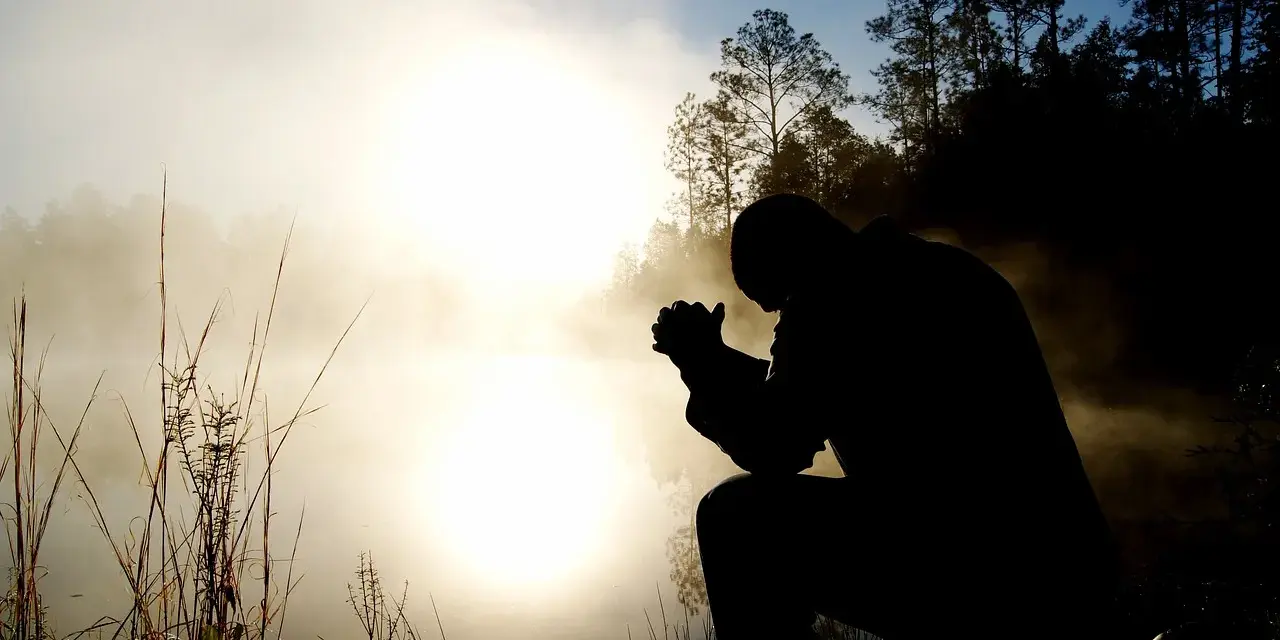Silhouette eines Mannes, der im Morgennebel kniet und betet. Ein Bild, das christliche Glaubensbekenntnisse widerspiegelt.