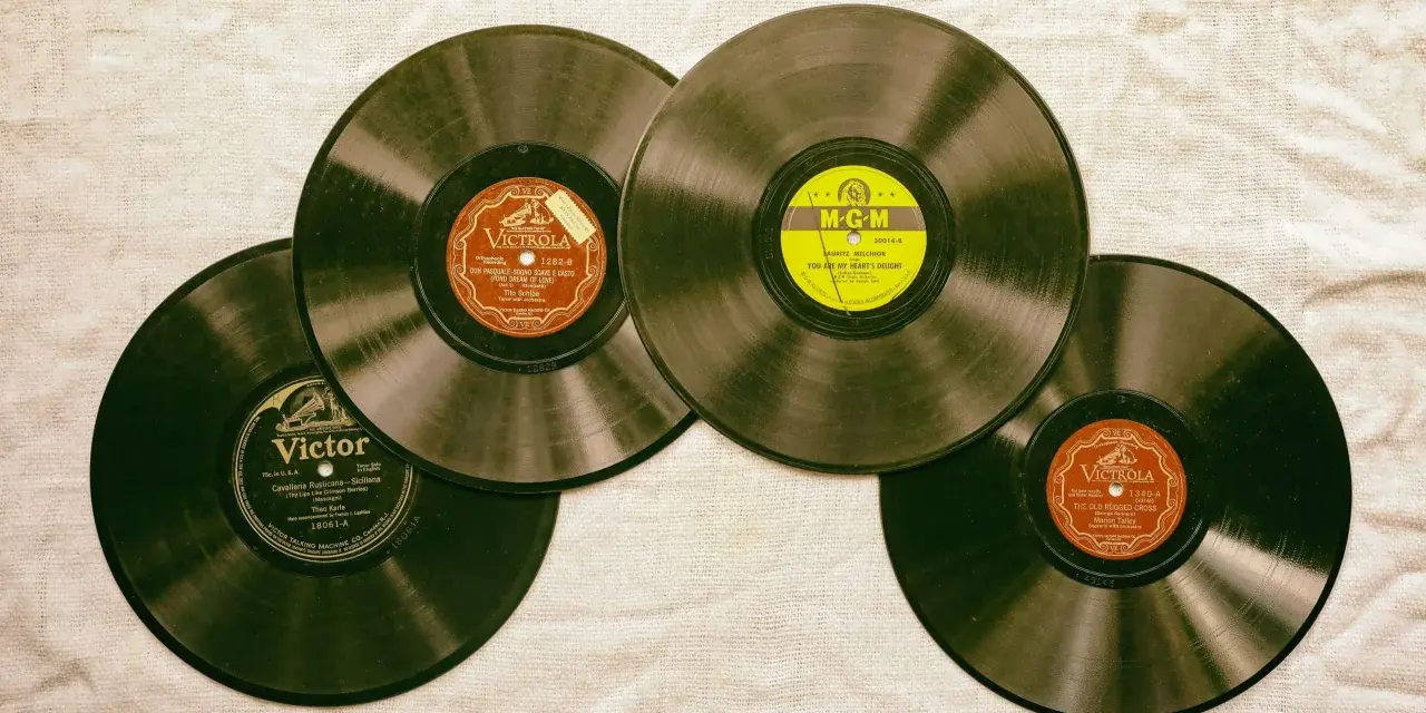 Vier alte Schallplatten liegen auf einer Leinwand. Eine davon hat ein gelbes MGM-Label, die anderen sind von Victrola und Victor. Sie erinnern an die Anfänge des Rocken Roll.