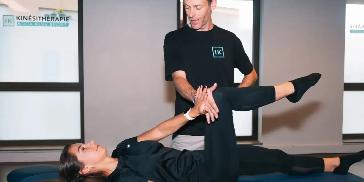 Un kinésithérapeute guide une patiente dans un exercice pour soulager la cruralgie. Elle est allongée sur une table de massage, une jambe pliée, l'autre tendue.