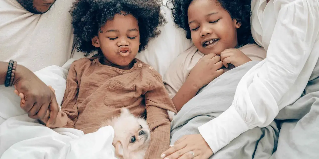 Familie kuschelt im Bett, um sich mit Kindern zu entspannen. Ein kleiner Hund liegt zwischen ihnen.