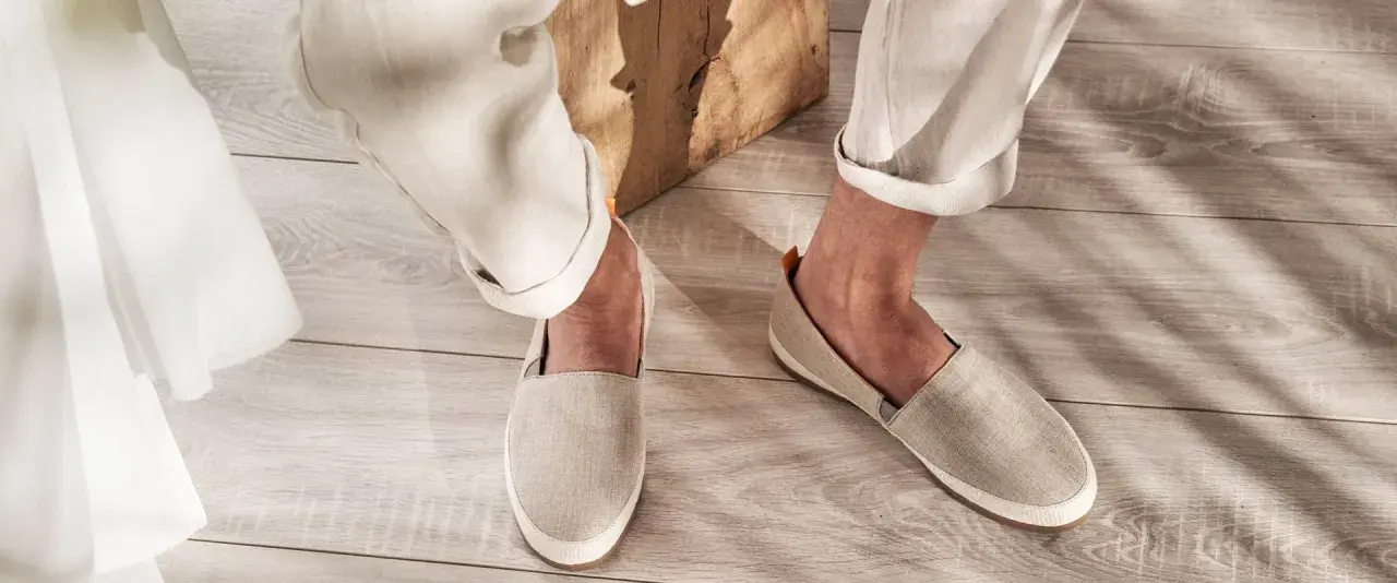 Un uomo indossa espadrillas in tela beige con pantaloni chiari arrotolati. Perfette per un look casual estivo, scopri come abbinarle.