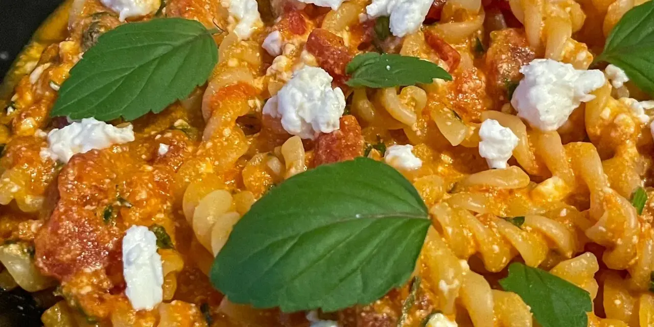Makaron fusilli w pomarańczowym sosie z kawałkami sera i listkami bazylii.