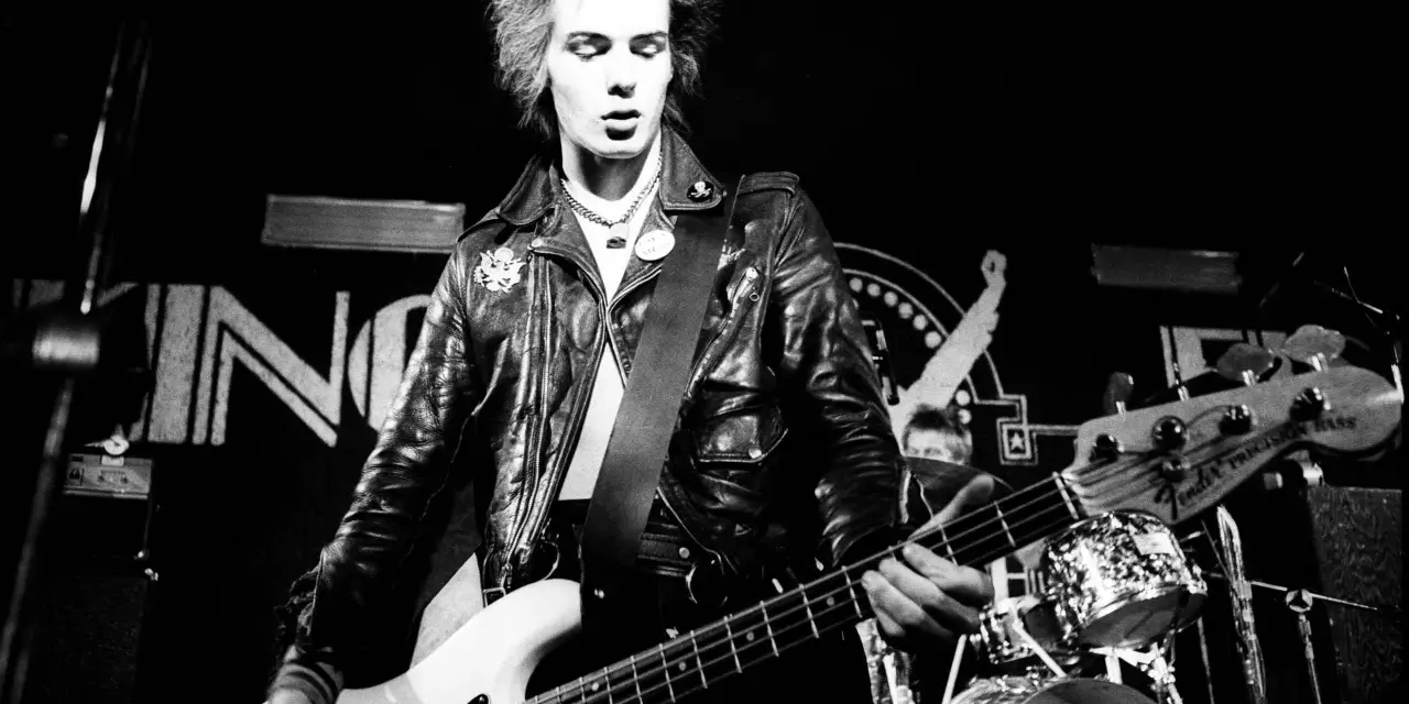 Sid Vicious, Punk-Ikone, spielt Bass auf der Bühne. Seine wilden Haare und Lederjacke unterstreichen seine rebellische Ausstrahlung. Seine Musik erfüllt die "sid wishes" des Publikums.