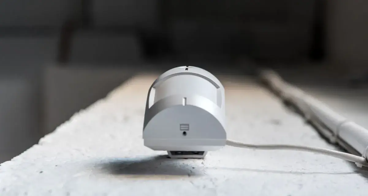Detector de presencia y movimiento blanco, con cable, montado en superficie rugosa.