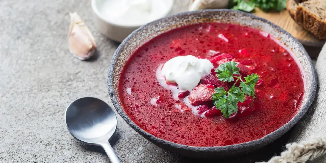Aromaticzny barszcz czerwony domowy z łyżką śmietany i natką pietruszki, obok czosnek i chleb.