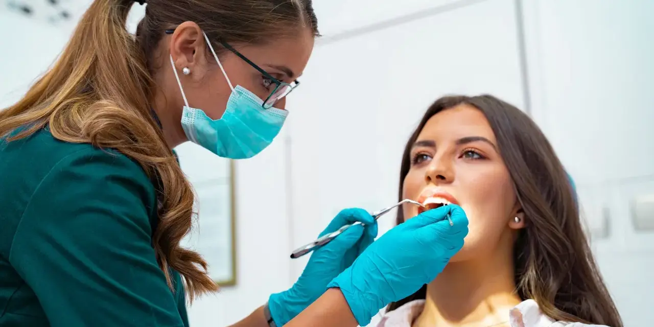 Dentystka w masce i rękawiczkach bada zęby pacjentki. To nie jest wyrywanie 8, ale rutynowa kontrola.