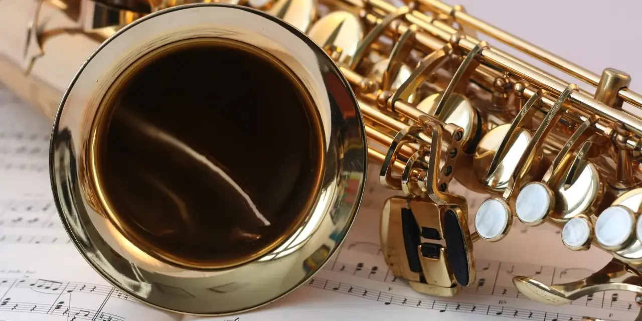 Ein glänzendes Musikinstrument, ein Saxophon, liegt auf Notenblättern. Seine goldene Oberfläche reflektiert das Licht.