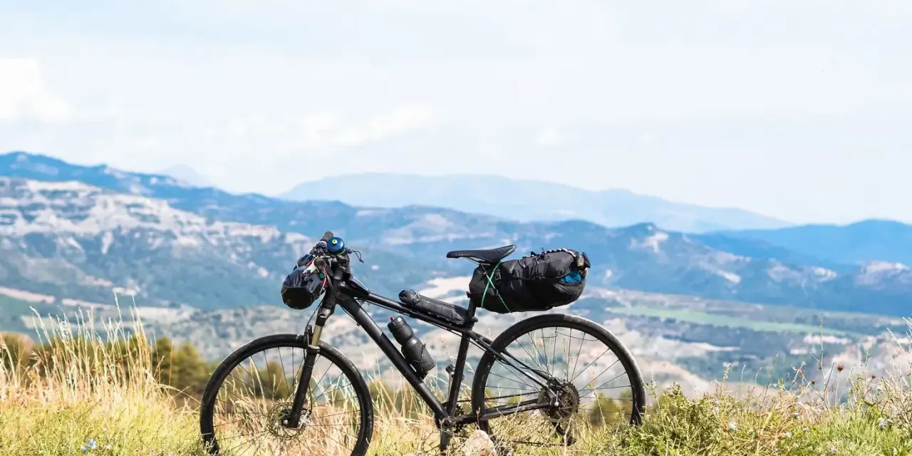 Rower gotowy do bike packingu, z sakwami na kierownicy i pod siodełkiem, na tle górskiego krajobrazu.