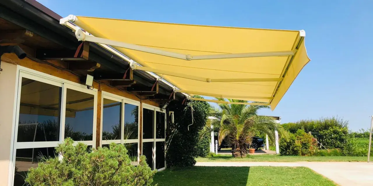 Tende da sole sconto in fattura, gialle e moderne, proteggono un edificio con ampie vetrate da un sole splendente.