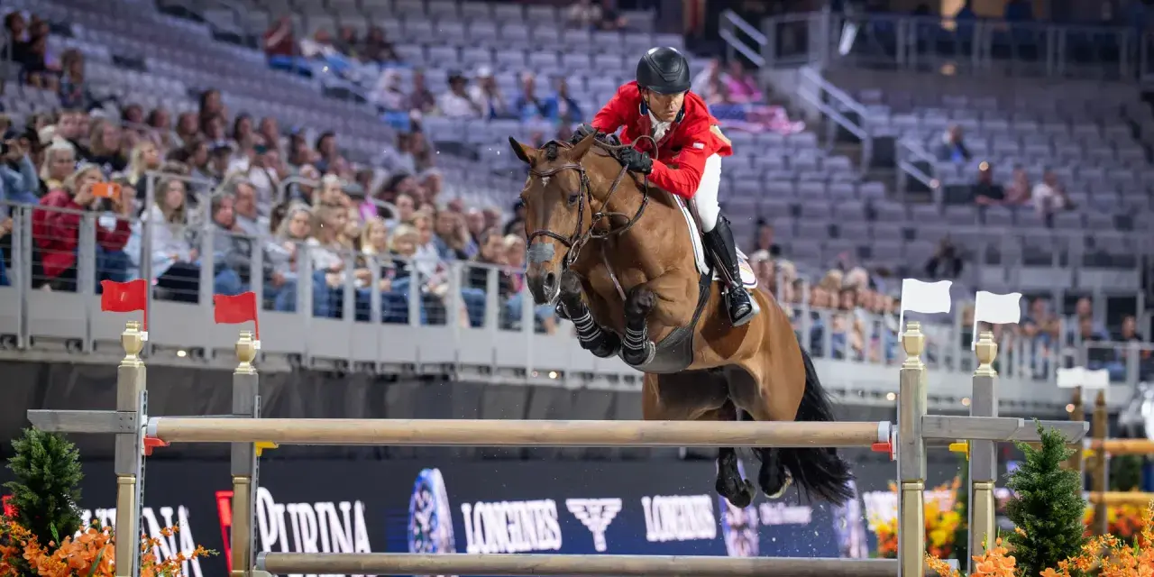 Cavalier en tenue rouge saute un obstacle lors d'une compétition équestre, visant la victoire à la **equestrian cup**.