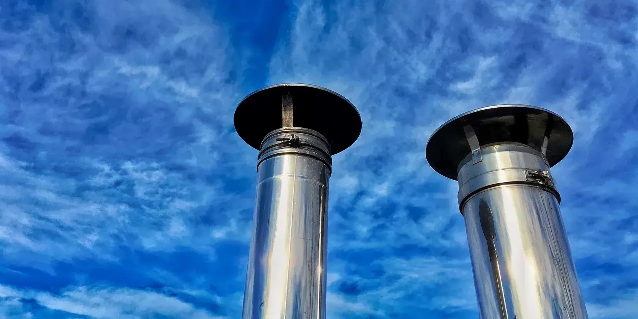Due camini in acciaio inox, modello uni 7129 scarico a parete, brillano sotto un cielo blu con nuvole sottili.