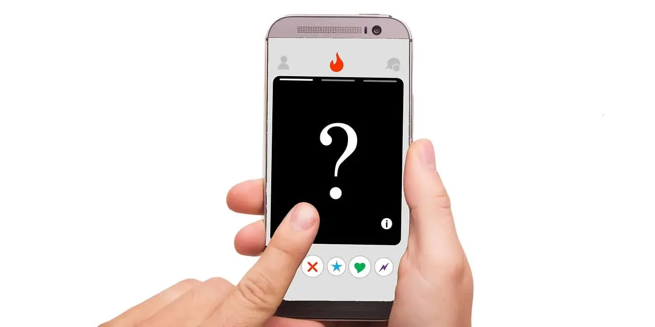 Dłoń trzyma smartfon z aplikacją randkową. Na ekranie widnieje znak zapytania i ikony: X, gwiazdka, serce, błyskawica. To **Tinder oznaczenia** – decyzja należy do Ciebie!