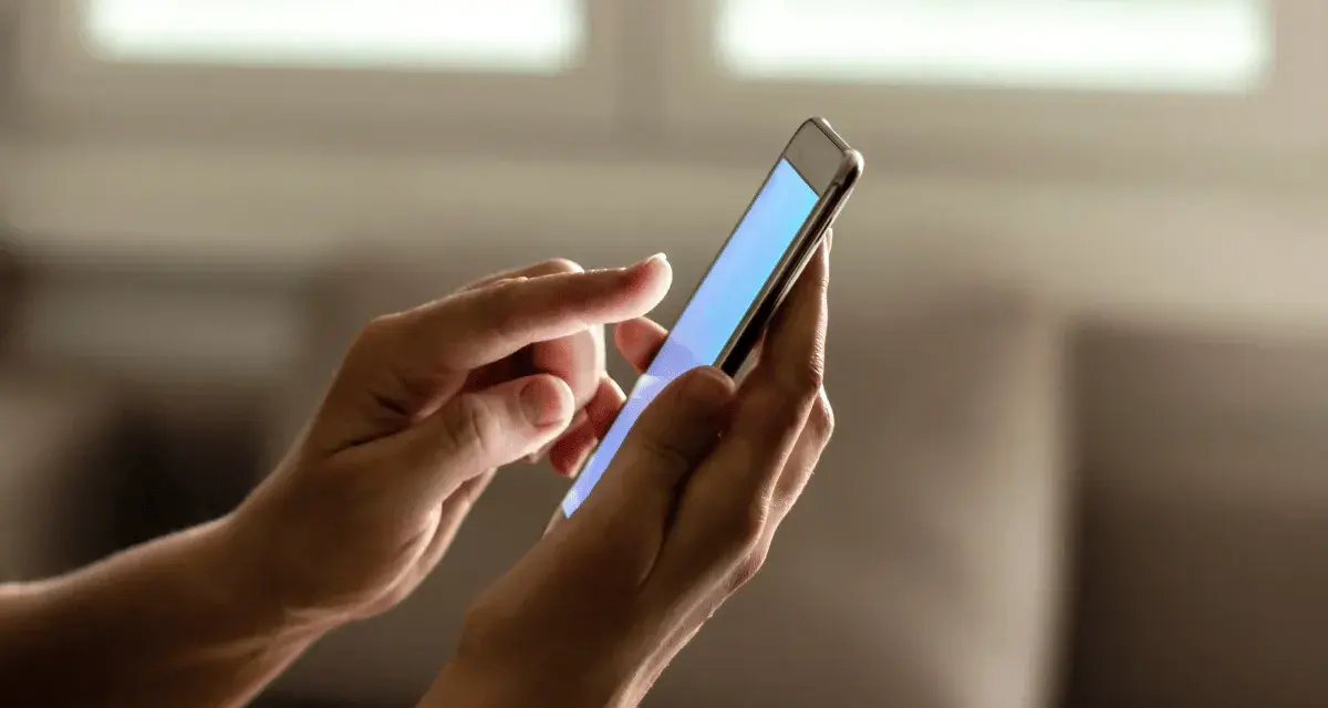 Dłonie trzymają smartfon, na ekranie którego wyświetla się niebieski kolor. Zastanawiasz się, jak sprawdzić ile lat ma telefon?