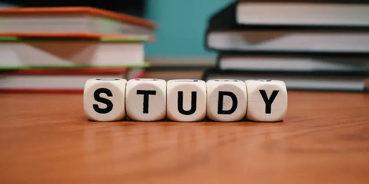 Kostki z literami "STUDY" na drewnianym blacie, obok stosów książek. Idealny temat rozprawki dla każdego ucznia.