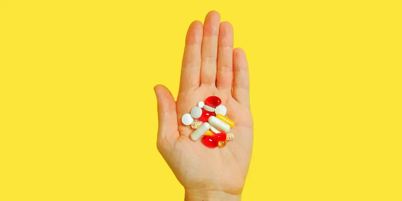 Hand hält bunte Pillen und Kapseln, die bei der Behandlung von Akne helfen könnten, wie z.B. Vitamin B5.