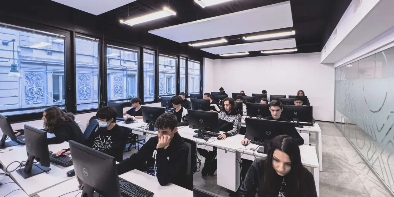 Giovani studenti concentrati davanti ai computer, un'aula moderna che ospita un corso di programmazione gratis.