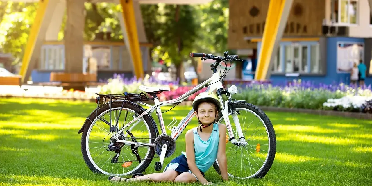 Dziewczynka w kasku odpoczywa obok roweru na trawie, gotowa na przygodę na szlaku EuroVelo 6.