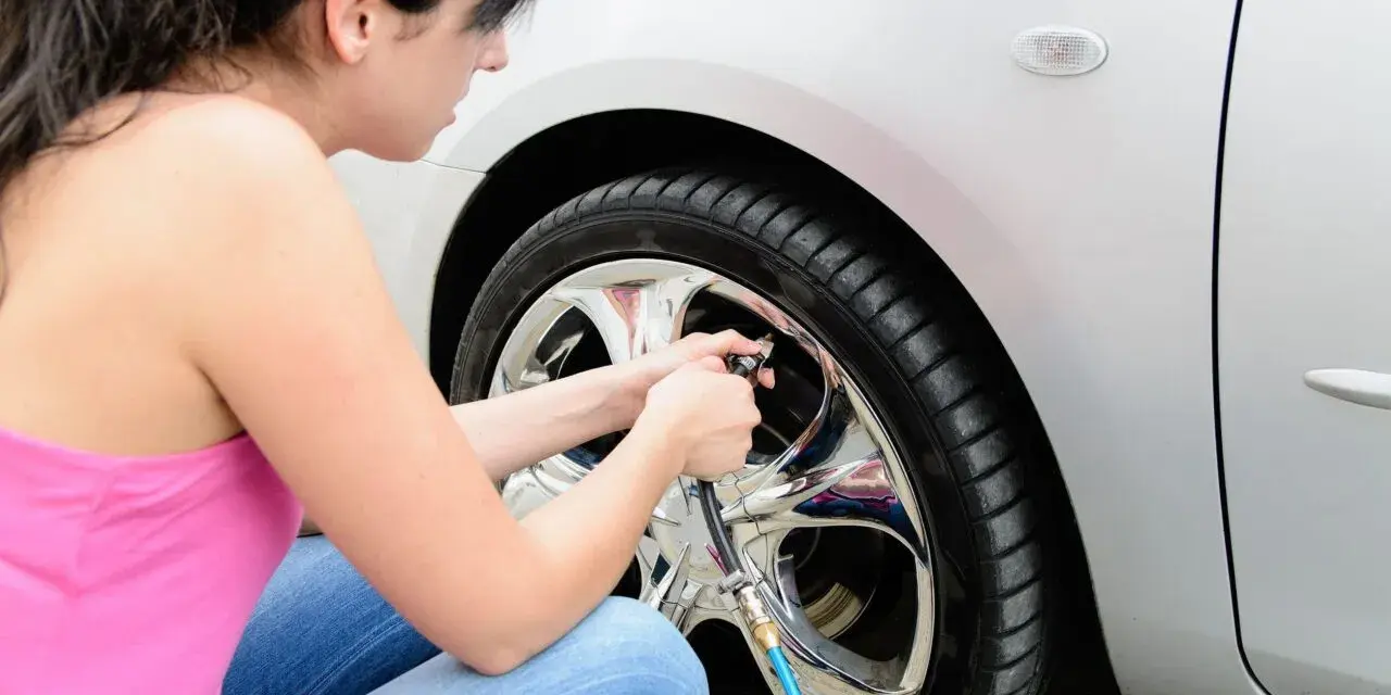 Donna in jeans e canotta rosa usa un compressore per gonfiare le gomme dell'auto, assicurandosi che siano alla pressione giusta.